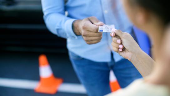 One person handing a driver's license to a teen driver