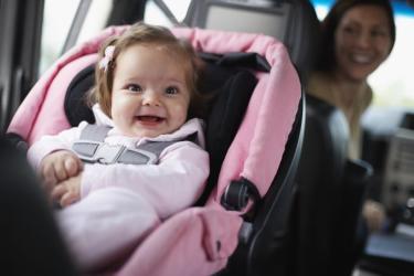 Smiling baby in pink car seat with parent smiling from front seat 